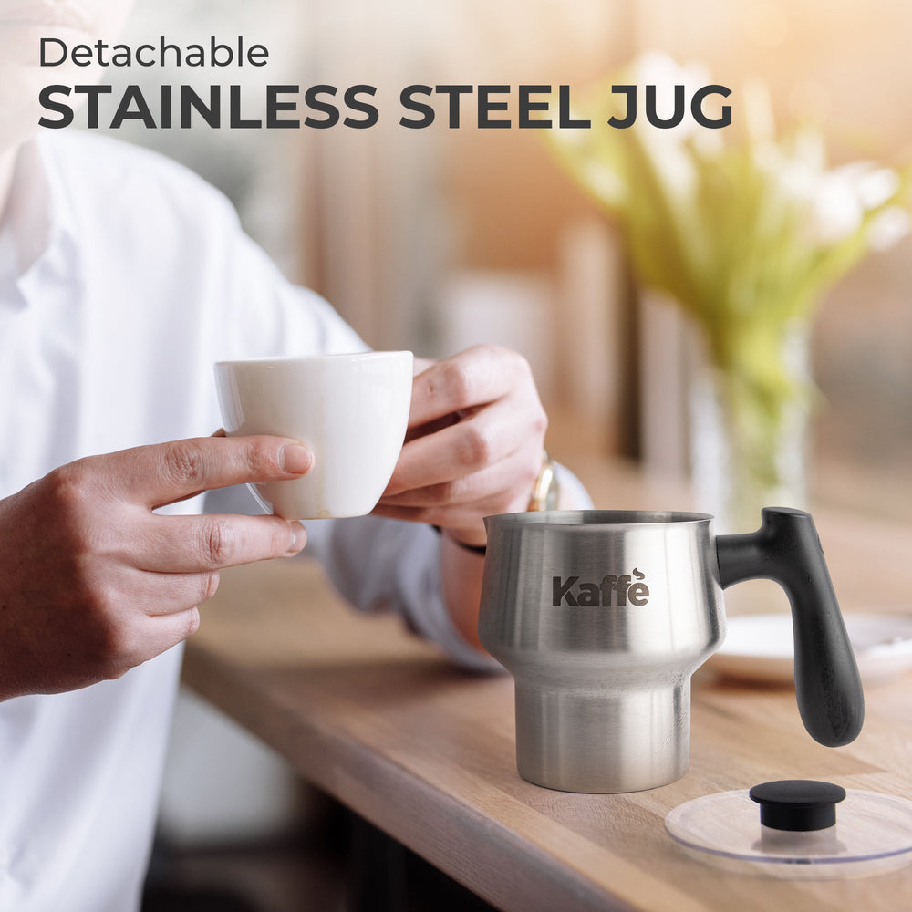 Person holding a white mug with a detachable stainless steel jug labeled 'Kaffe' on a wooden surface.