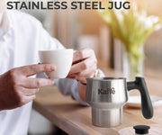 Person holding a white mug with a detachable stainless steel jug labeled 'Kaffe' on a wooden surface.